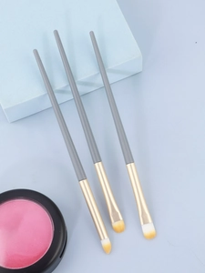 Detailed view of three gray makeup brushes with gold ferrules and a pink powder compact