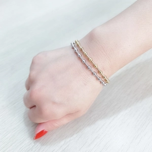 Detail view of gold and silver elastic beaded bracelets on a model wrist over wood
