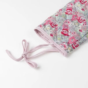 Detail of quilted floral cotton sleeve with pink stripe ties and bow on a white background