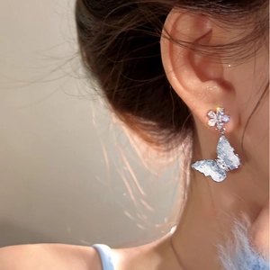Detail shot of elegant blue butterfly drop earrings with flower studs worn on ear