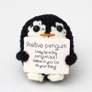 Detail of hand-knitted penguin doll holding a positive message card on white background