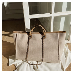 Detailed texture of beige canvas tote bag with brown leather trim and chain strap