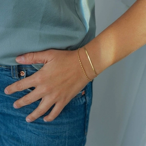 Close-up of a lady wearing stacked gold snake and bead chains on the wrist in natural light