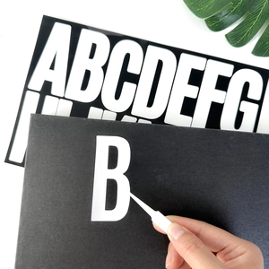 Close-up of using tweezers to apply a black 3-inch vinyl letter B sticker for DIY decor
