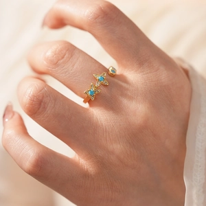 Gros plan d'une bague ouverte dorée avec trèfles sertis de turquoise et diamants