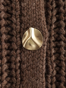 Detail of a wavy gold metal button on a brown chunky knit wool sweater vest