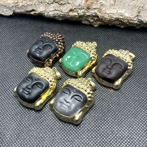Fashionable Buddha head pendants with gold and copper trim on a textured black surface