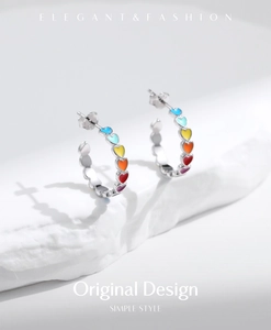 Detail of silver S925 heart earrings with rainbow enamel on a white stone display