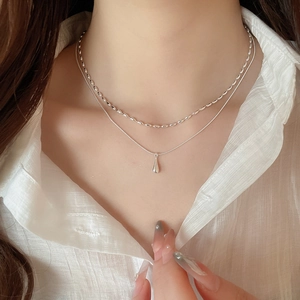 Detail of layered silver teardrop necklace on model with elegant chiffon shirt