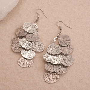 Silver layered teardrop earrings with textured metal discs on a minimalist beige background