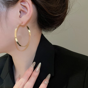 Close-up of oversized flat wide-edge gold hoop earrings worn by a model in a black suit