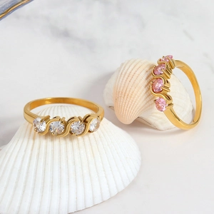 Minimalist gold wave rings with white and pink cubic zirconia on a decorative shell
