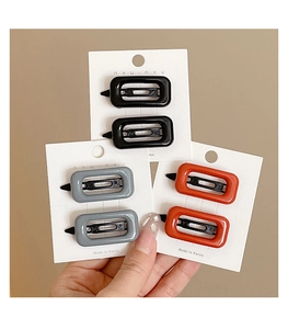 Three pairs of rectangular hair clips in black, grey and orange-red on white cards