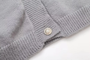Details des grauen Strick-Cardigans mit geprägten Goldknöpfen und weicher Textur
