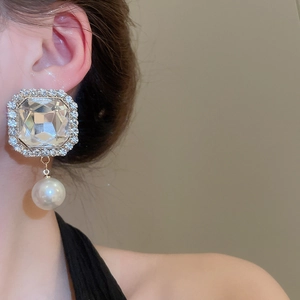 Detail of square-cut rhinestone earrings with drop pearls on elegant model