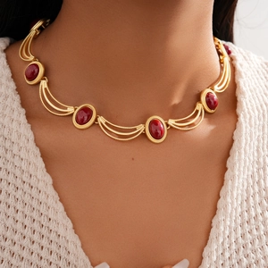 Gros plan d'un collier doré vintage avec gemmes rouges sur un pull en maille
