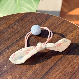 Floral bow scrunchie with light blue bead accent on dark wood background