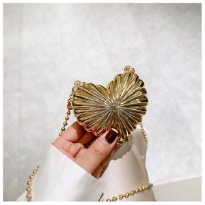 Detail of golden heart-shaped mini metal shell bag with radial texture and beaded chain