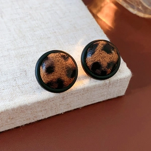 Gros plan de boucles d'oreilles rondes léopard avec cadre noir sur lin beige