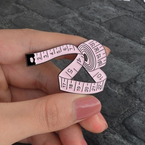 Detailed view of hand-held pink tape measure enamel brooch with scale markings
