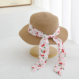 Detail of flat top straw hat featuring a cherry print ribbon and long streamers