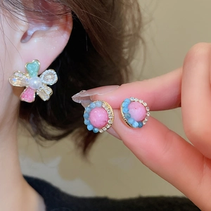 Close-up of floral crystal earrings and round pink stone studs with pearl accents