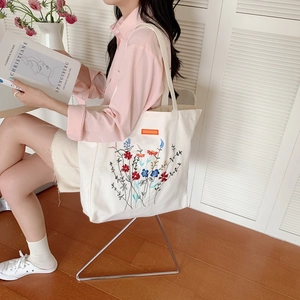 Detailed close-up of vibrant floral embroidery on a minimalist beige canvas tote bag