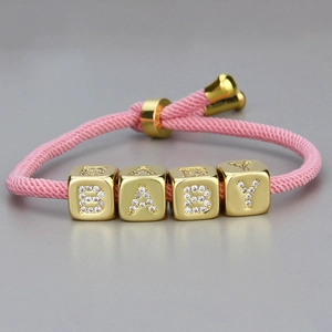 Nahaufnahme vom rosa geflochtenen Armband mit goldenen BABY-Buchstabenwürfeln