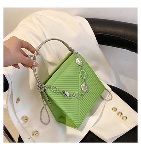Detail of light green textured handbag with round silver handle and chain on white blazer