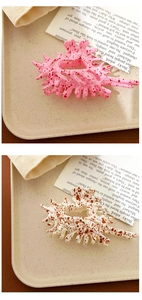 Close-up of pink and cream seashell-shaped hair claws with coral spots on an open book