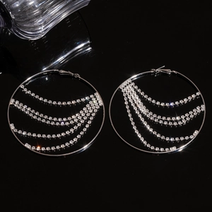 Silver fringe hoop earrings with glittering rhinestones on a sleek black reflective surface