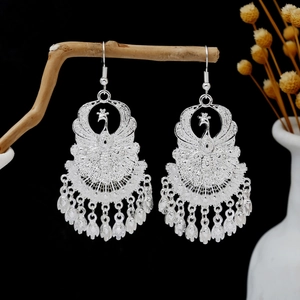 Detailed close-up of peacock earrings with silver tassels on a rustic branch