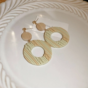Detail of round woven earrings with beige and mint green stripes on a ceramic plate