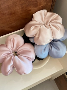 Detailed texture of satin flower scrunchies in pink, champagne and blue on a tray
