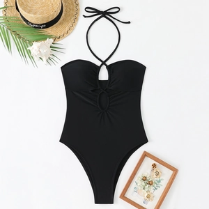 Maillot de bain noir à licou et découpe avec chapeau de paille et feuilles de palmier