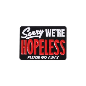 Square enamel pin badge featuring 'Sorry WE'RE HOPELESS PLEASE GO AWAY' text on black