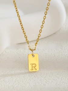 Gros plan sur un pendentif carré doré avec la lettre R sur une fine chaîne dorée