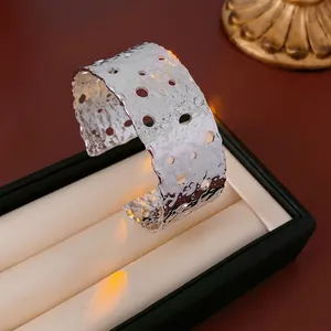 Polished silver textured open cuff bracelet with circular hollow cut-outs in a jewelry box