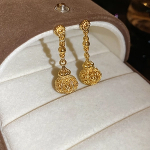Macro shot of gold hollow ball earrings with intricate texture in a brown velvet gift box