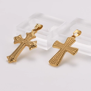Two golden stainless steel cross pendants with vintage embossed textures on a white stand