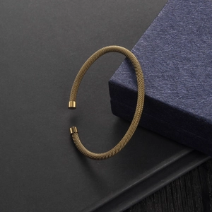 Close-up of golden mesh cable bracelet with cylindrical end caps on a dark textured background