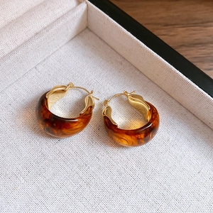 Detailed view of U-shaped amber resin earrings with polished gold metal finish