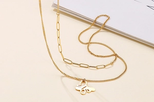 Close-up of golden double-layer necklace featuring butterfly pendant and paperclip chain
