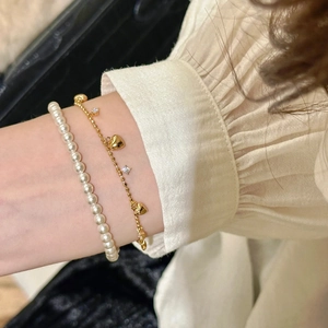 Dettaglio di bracciali sovrapposti con cuore dorato e perle bianche sul polso