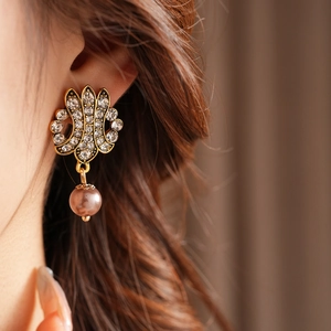 Close-up of vintage hollow gold earring with crystals and a pink pearl drop on model