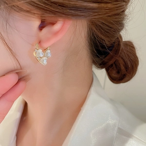 Detailed view of heart-shaped gold floral earrings with zircon and pearls on a model