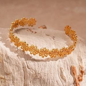 Macro shot of gold daisy flower cutout bracelet on stone showing intricate metal details