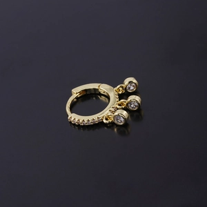 Gold plated rivet huggie hoop earring with dangling clear zircon stones on black surface