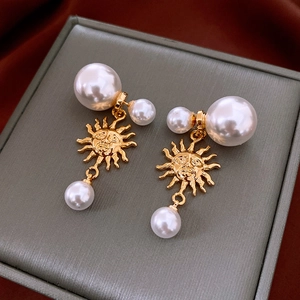 Close-up of golden sun face earrings with white pearls on a textured jewelry box surface