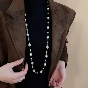 Close-up of elegant long pearl necklace layered over a black turtleneck and brown jacket